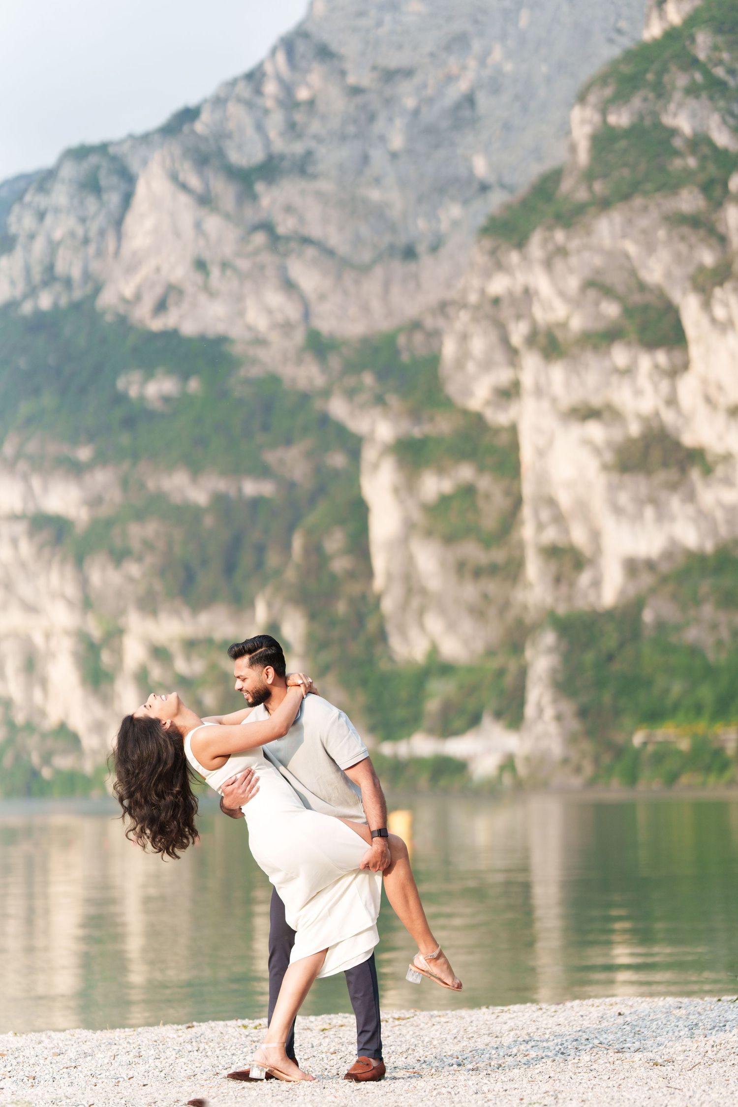 Romantic couple embracing by scenic mountain lake with dramatic limestone cliffs in background.