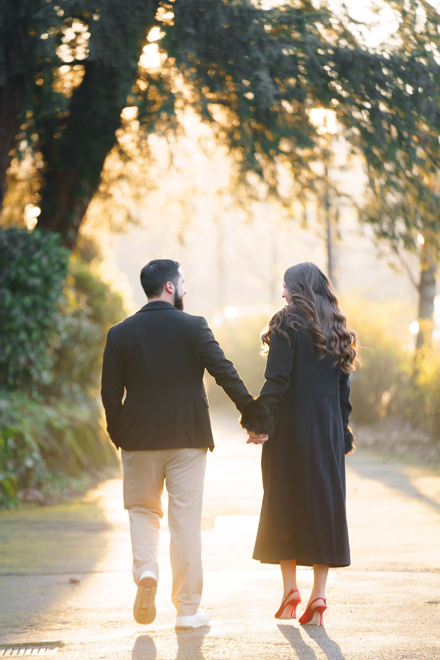 A couple walking together on a sunlit path through trees during golden hour creates a romantic silhouette.