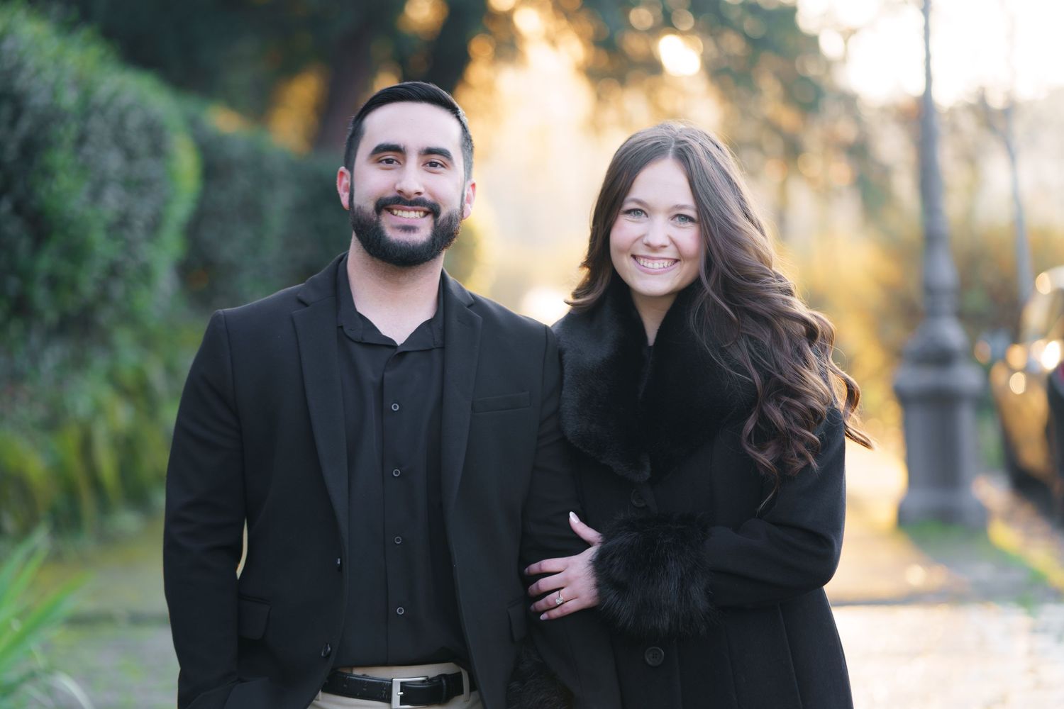 A couple wearing black outfits poses together outdoors during a golden sunset photoshoot in a natural setting.