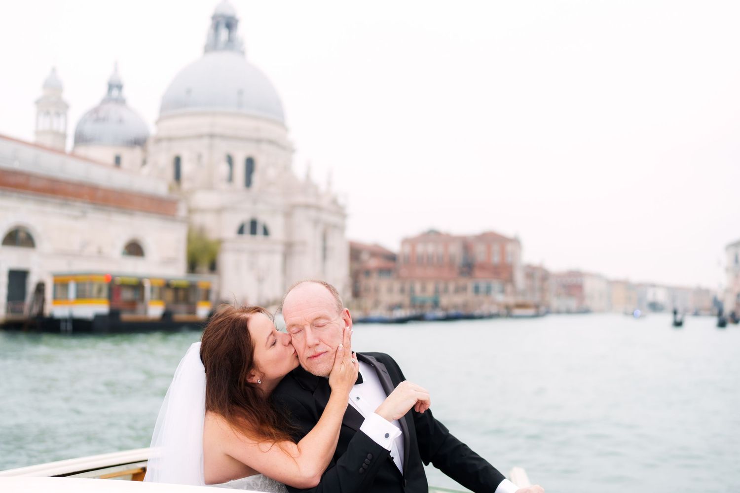 A romantic couple shares tender moments while sightseeing along the canals of Venice, Italy with gondolas in view.