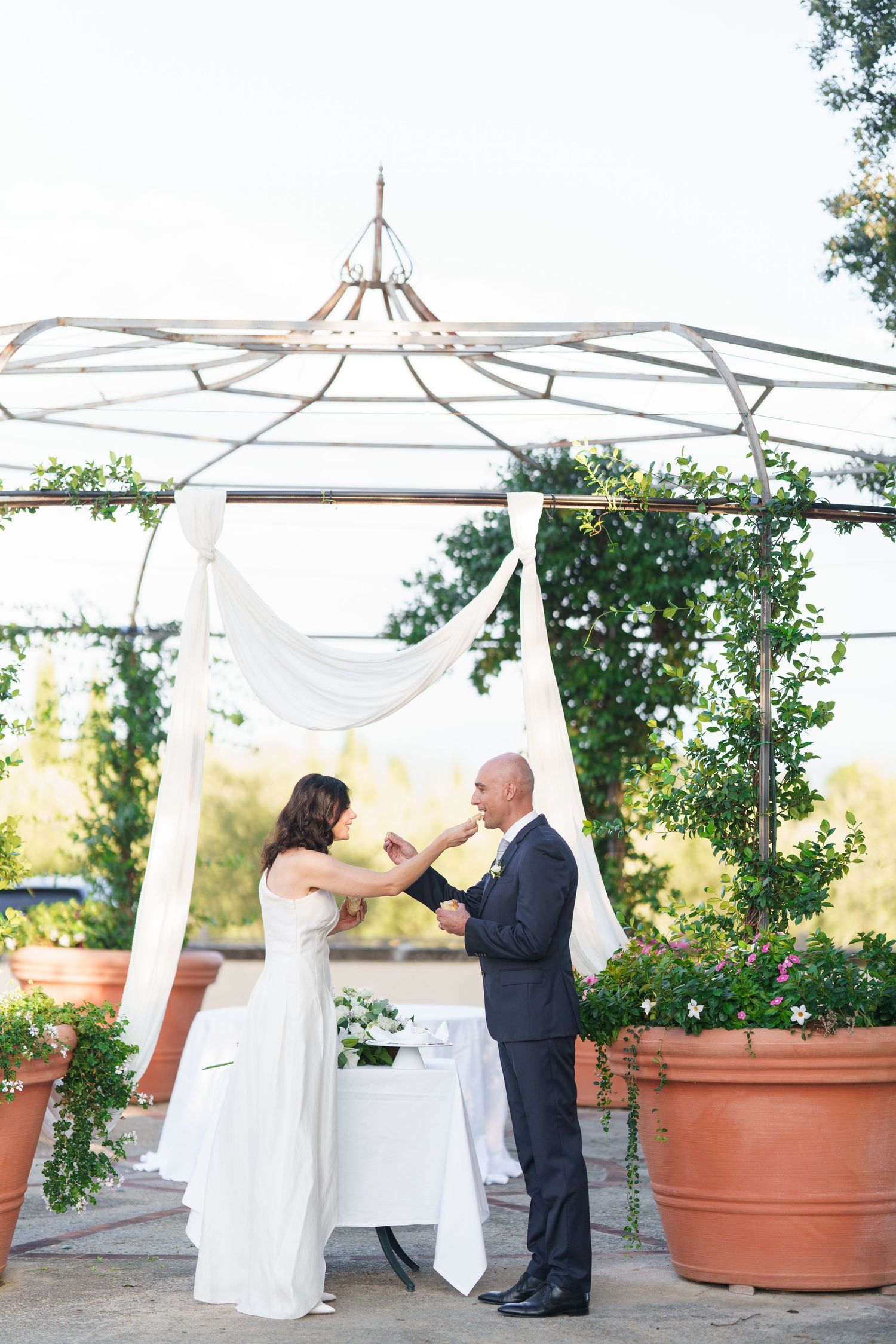 Wedding ceremony setup with white canopy and potted plants on outdoor terrace.