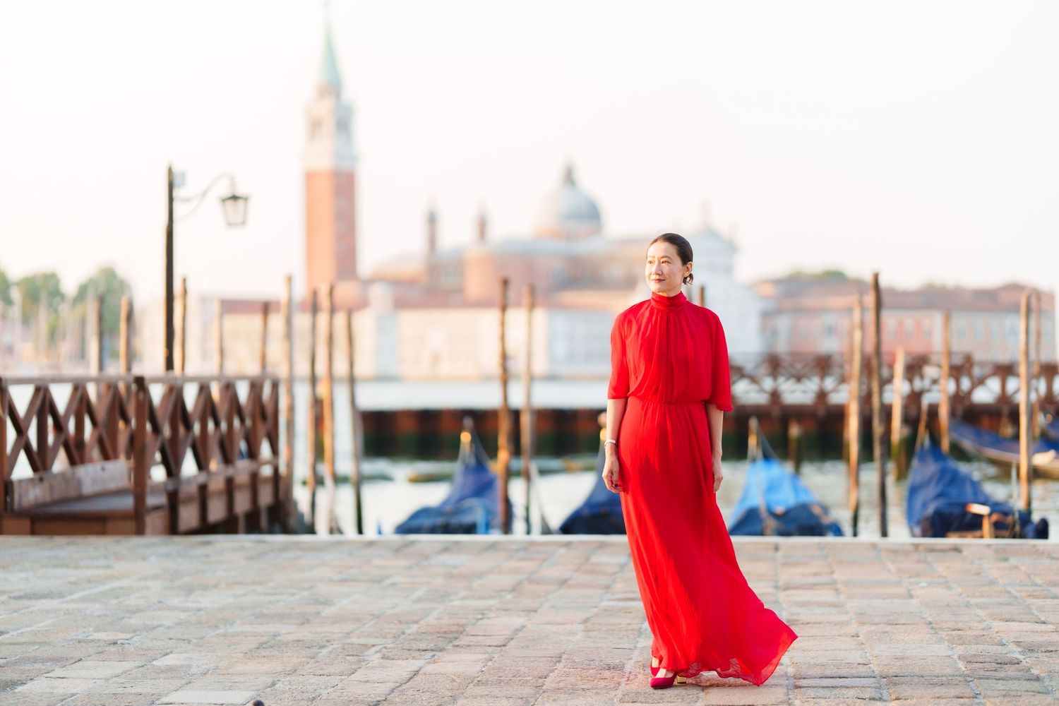 Woman in red dress standing by Venice Grand Canal with gondolas and San Giorgio Maggiore church in background.