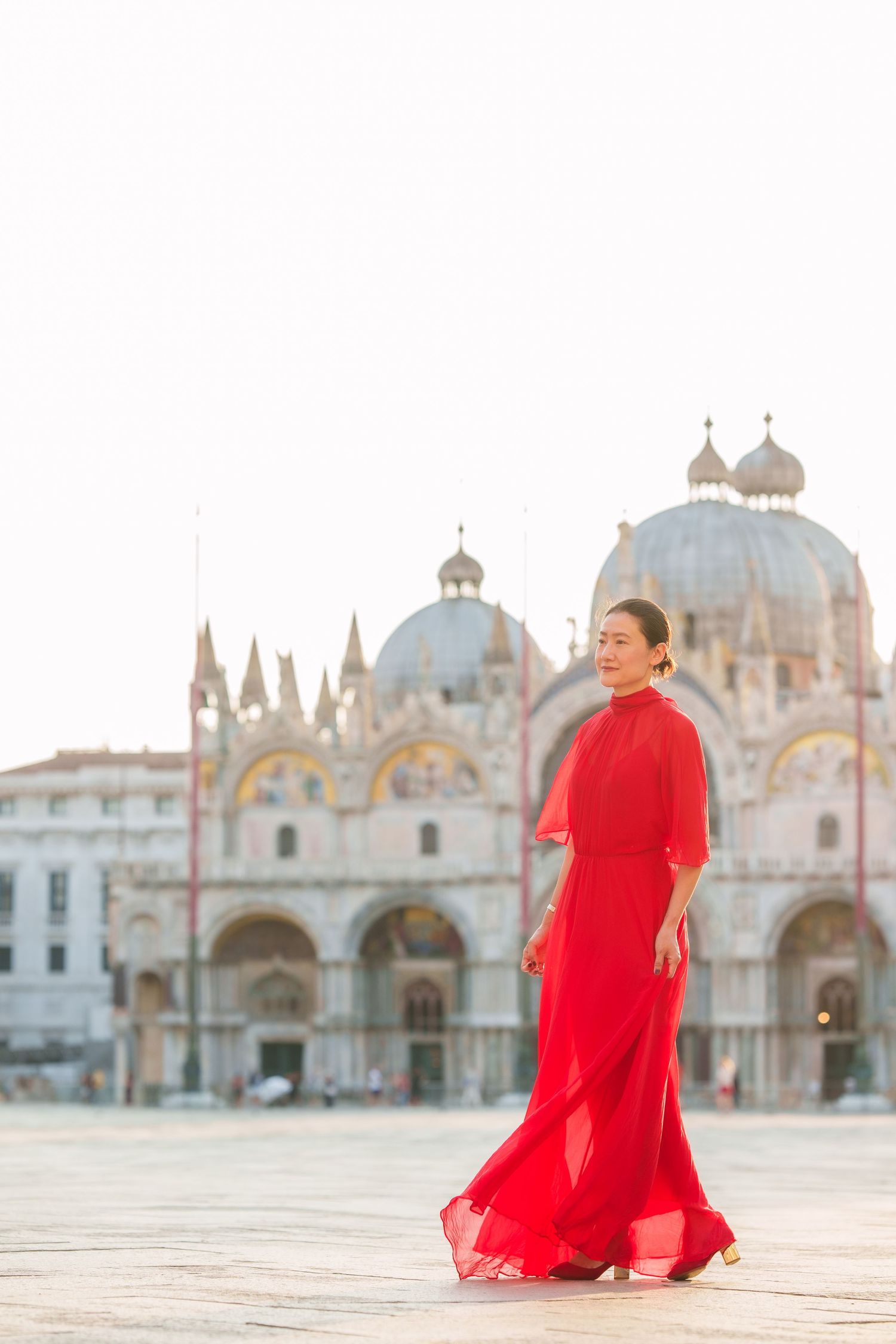 Woman in red dress at St. Mark's Square, Venice, with the iconic Basilica di San Marco in the background.