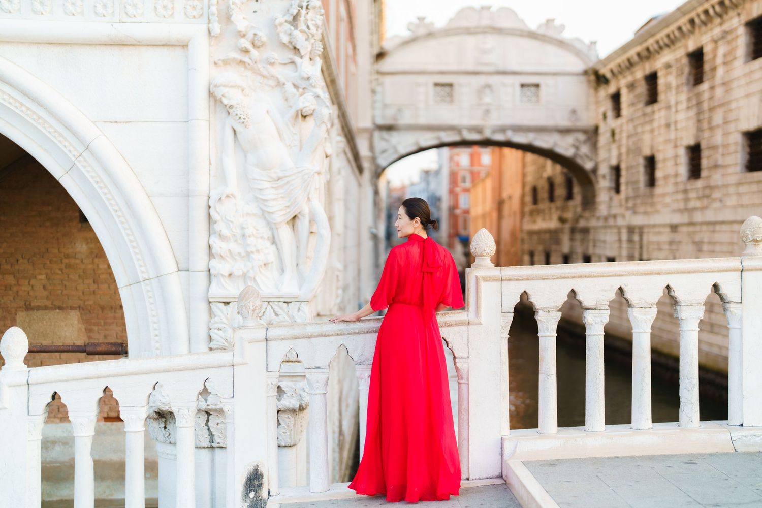 Woman in red gown stands on Venice bridge near Bridge of Sighs, Italy.