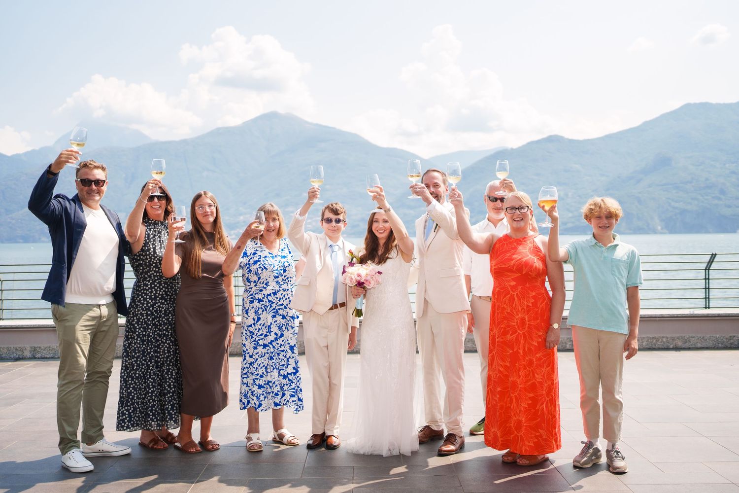Wedding party celebrating outdoors with champagne, mountains and lake in background on a sunny day.