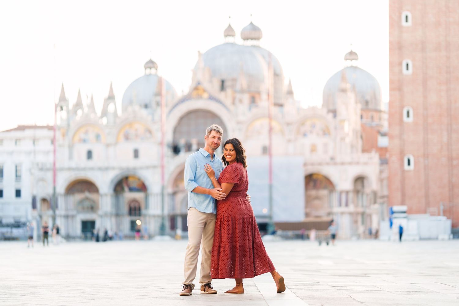 Couple embracing in Venice's St. Mark's Square with the iconic Basilica di San Marco in the background.