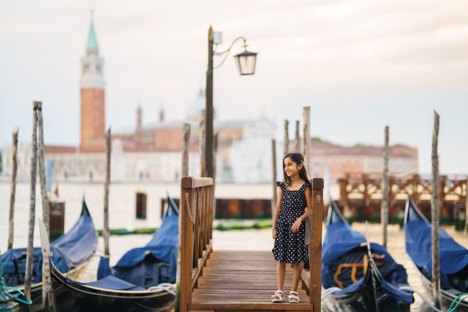 Woman in polka dot dress standing on a gondola pier in Venice, Italy, with San Giorgio Maggiore in background.