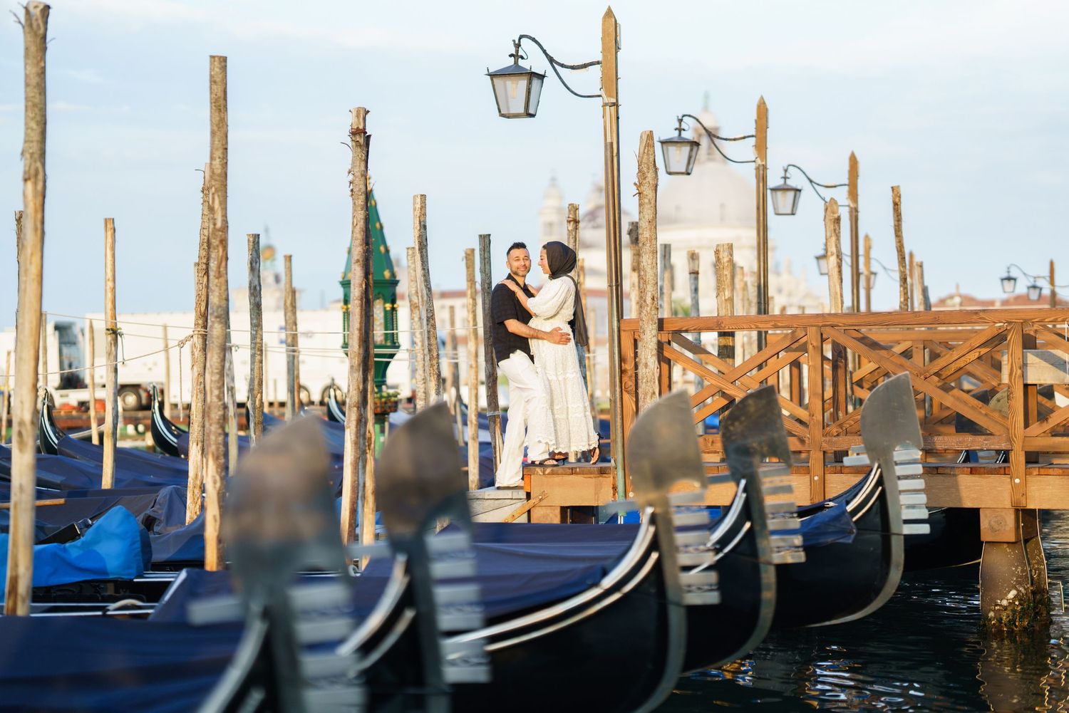 Couple embracing on Venice waterfront dock surrounded by gondolas at golden hour.