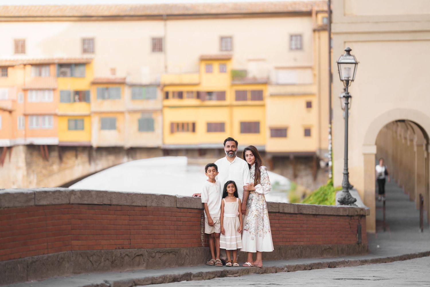 Family of four posing in front of Ponte Vecchio bridge in Florence, Italy, wearing elegant white outfits.