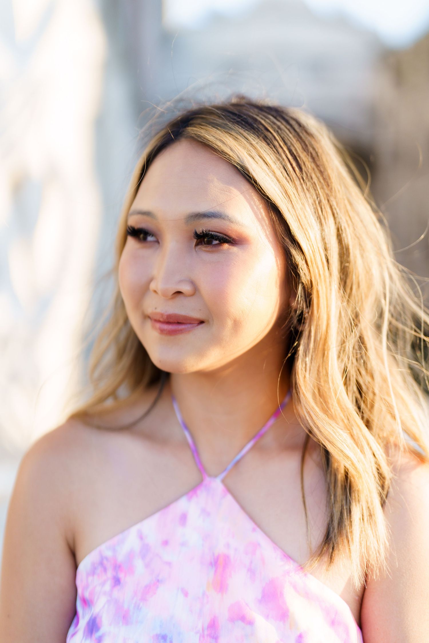 Young woman with blonde highlights wearing a pink floral halter top, posing outdoors in soft natural light.