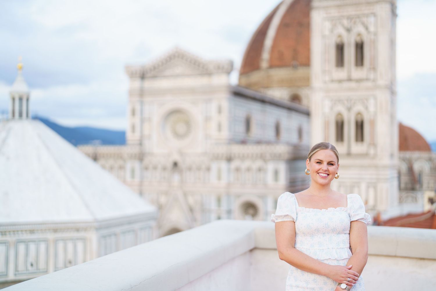 A bride in a white dress poses on a balcony overlooking Florence Cathedral and historic Italian architecture.