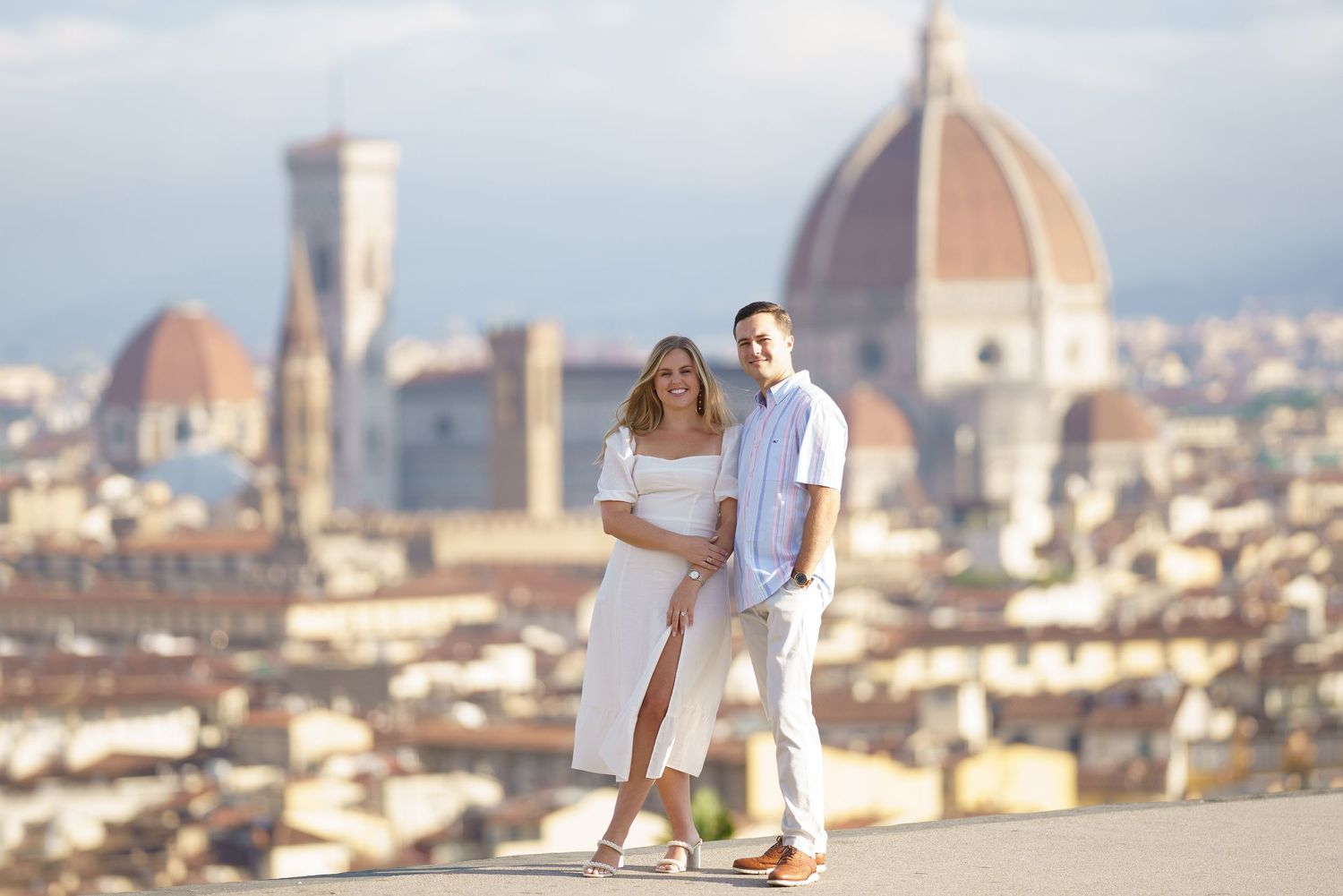 Couple in white outfits pose with scenic view of Florence's Duomo cathedral and cityscape in background.