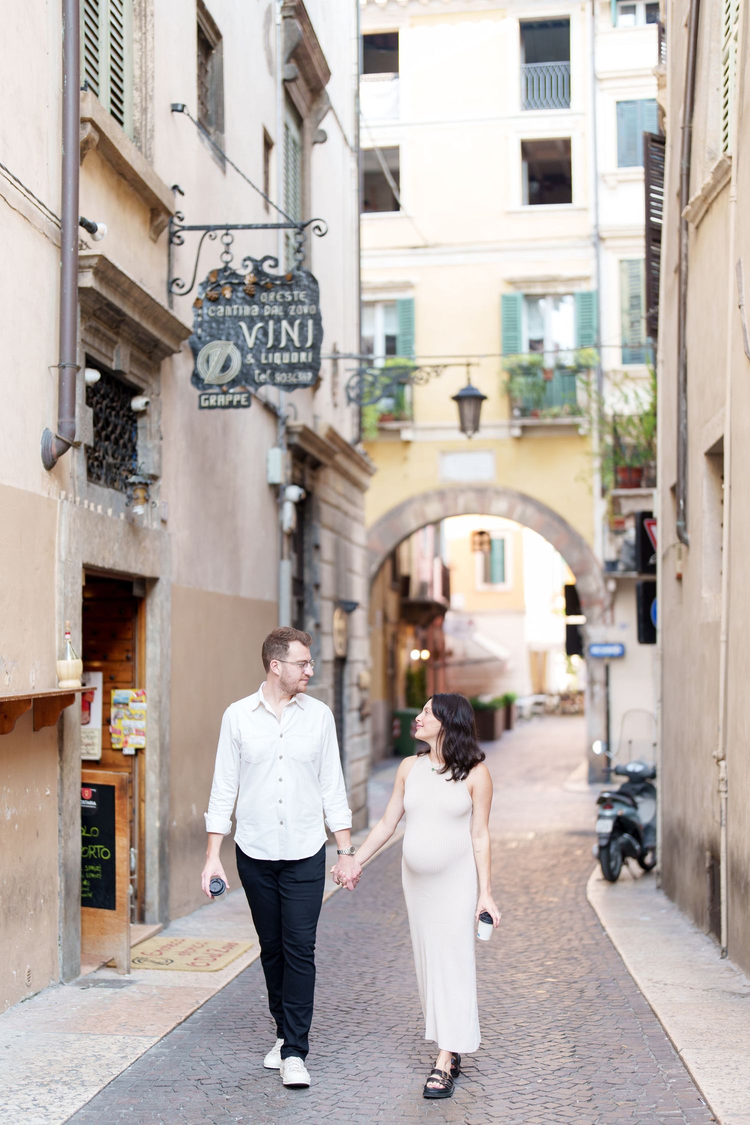 A couple walks hand in hand through charming European alleyways with stone buildings and archways.
