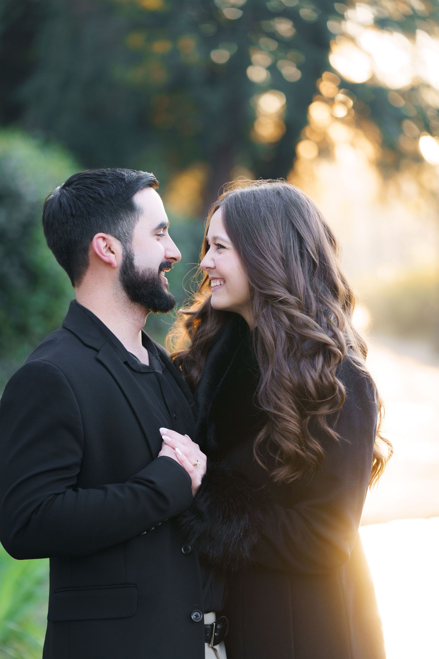 A couple shares a tender moment outdoors during sunset, their silhouettes backlit by golden light.
