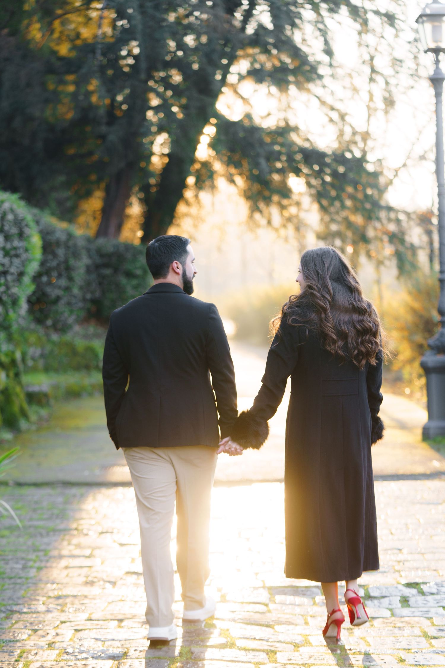 A couple walks together on a sunlit stone path during golden hour, creating a romantic silhouette against the warm light.