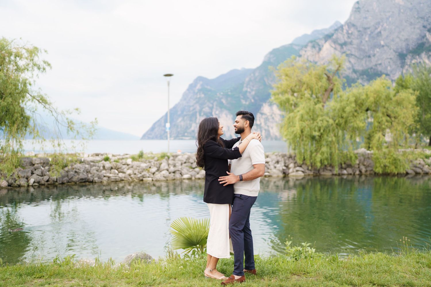 A couple shares a romantic moment by a scenic mountain lake surrounded by lush greenery and rocky cliffs.