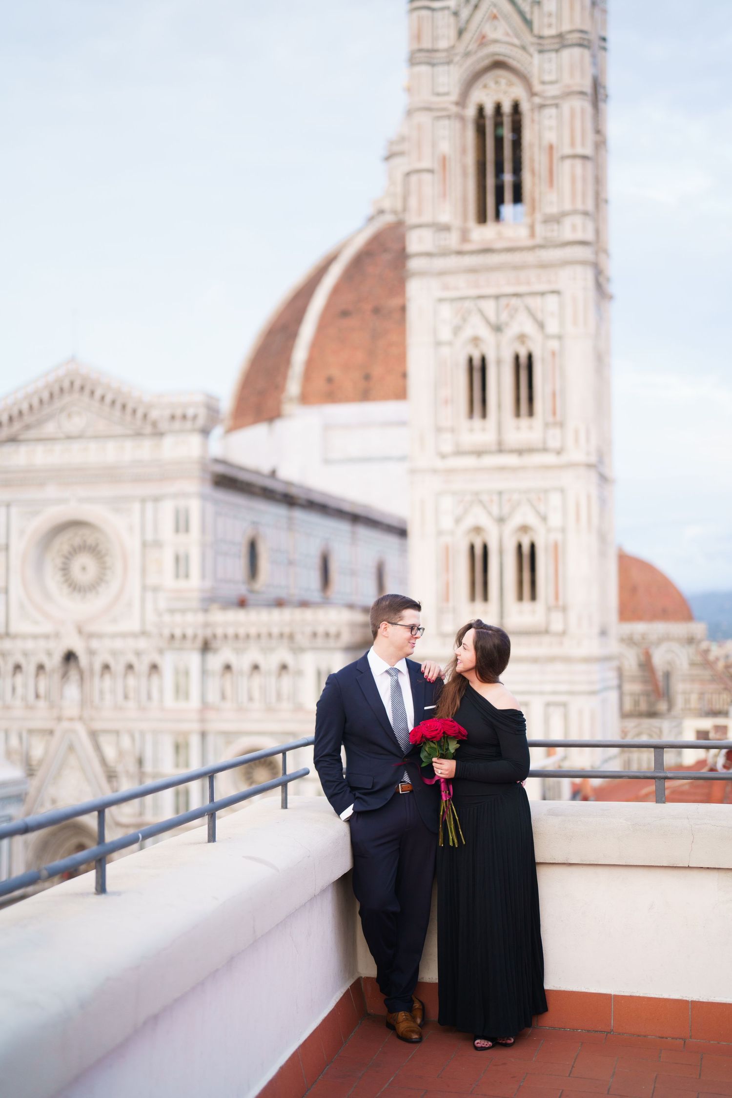A couple shares a romantic moment on a terrace overlooking Florence Cathedral's iconic dome and architecture.