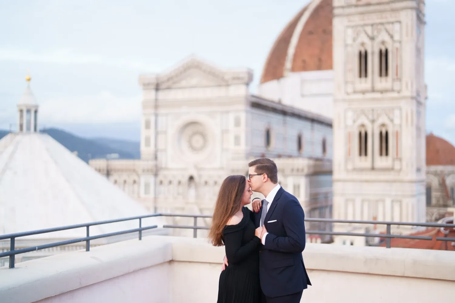 A couple shares a romantic moment on a balcony overlooking Florence's historic Duomo cathedral in Italy.