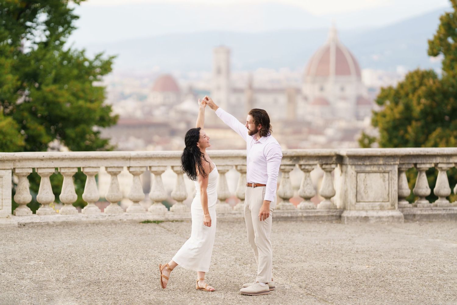 People walk along a scenic terrace overlooking Florence, Italy with the iconic Duomo cathedral dome visible in background.