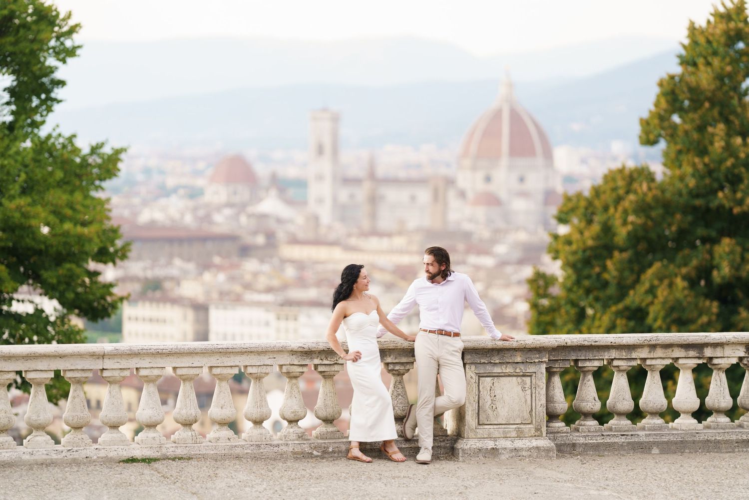 A couple enjoys a romantic moment overlooking the historic Florence cityscape from Piazzale Michelangelo at sunset.