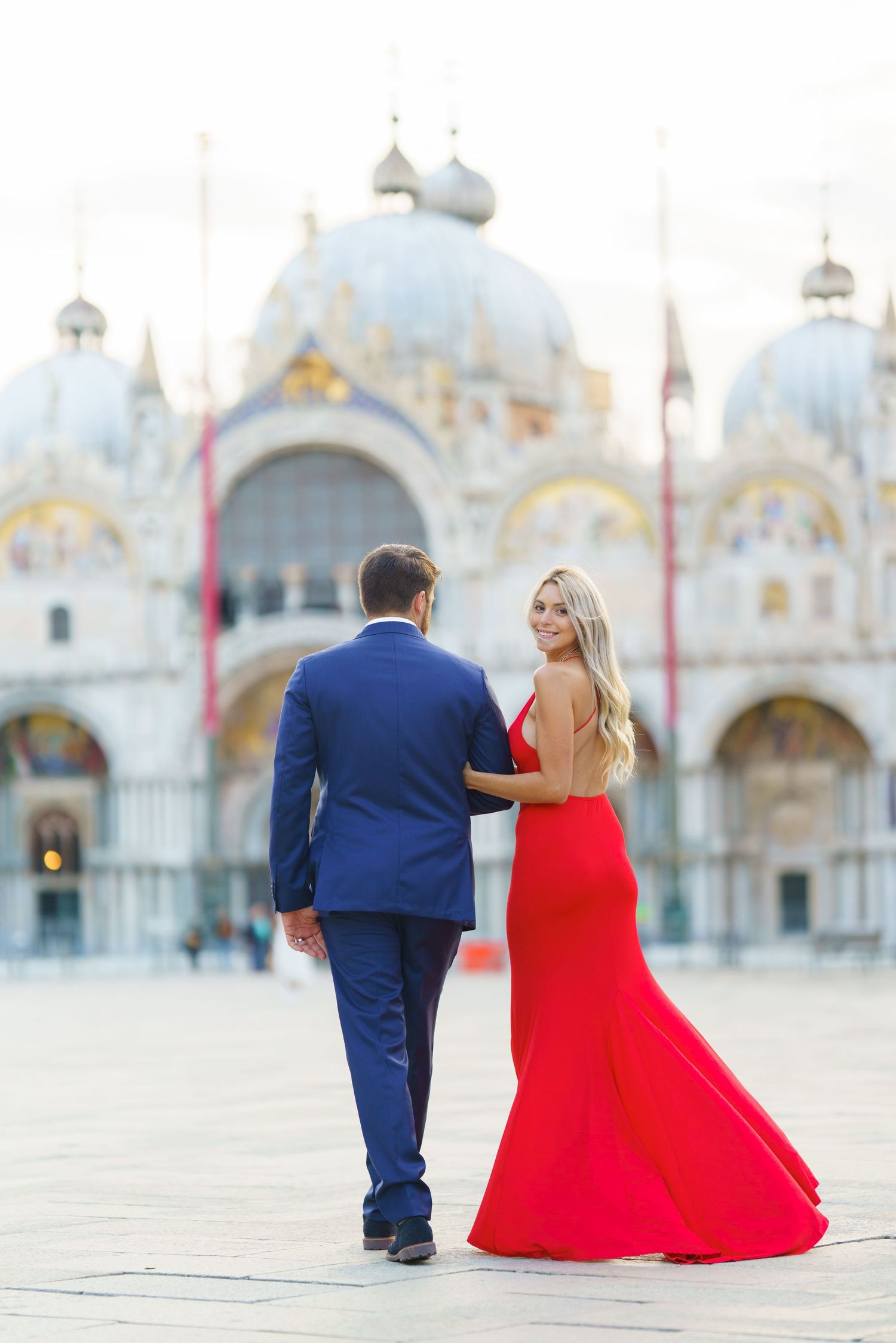 A couple in formal attire poses at St. Mark's Square in Venice with the basilica's ornate facade in the background.