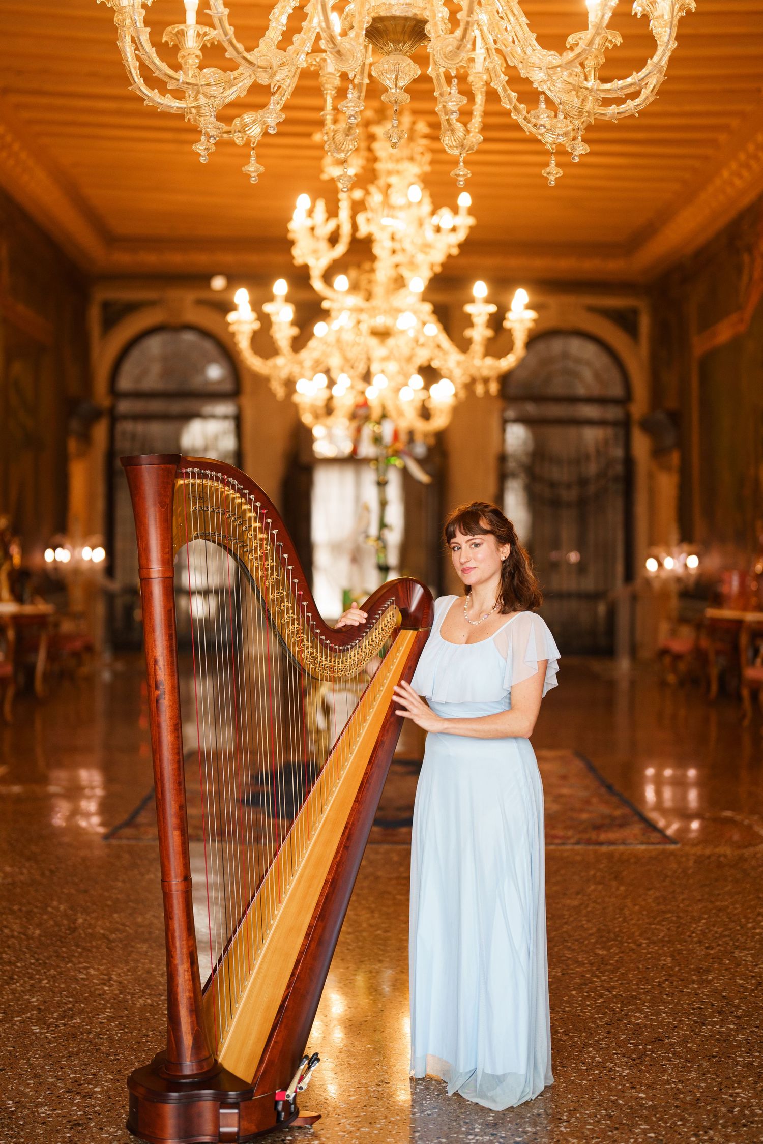 A harpist performs in an elegant ballroom with crystal chandeliers and ornate decor.