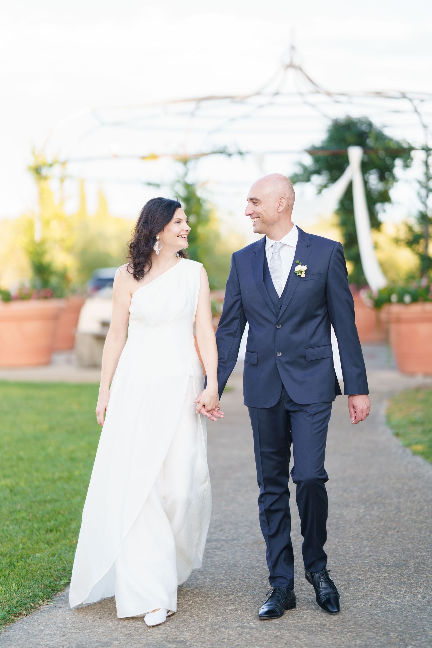 Wedding couple walking together on garden path during golden hour.