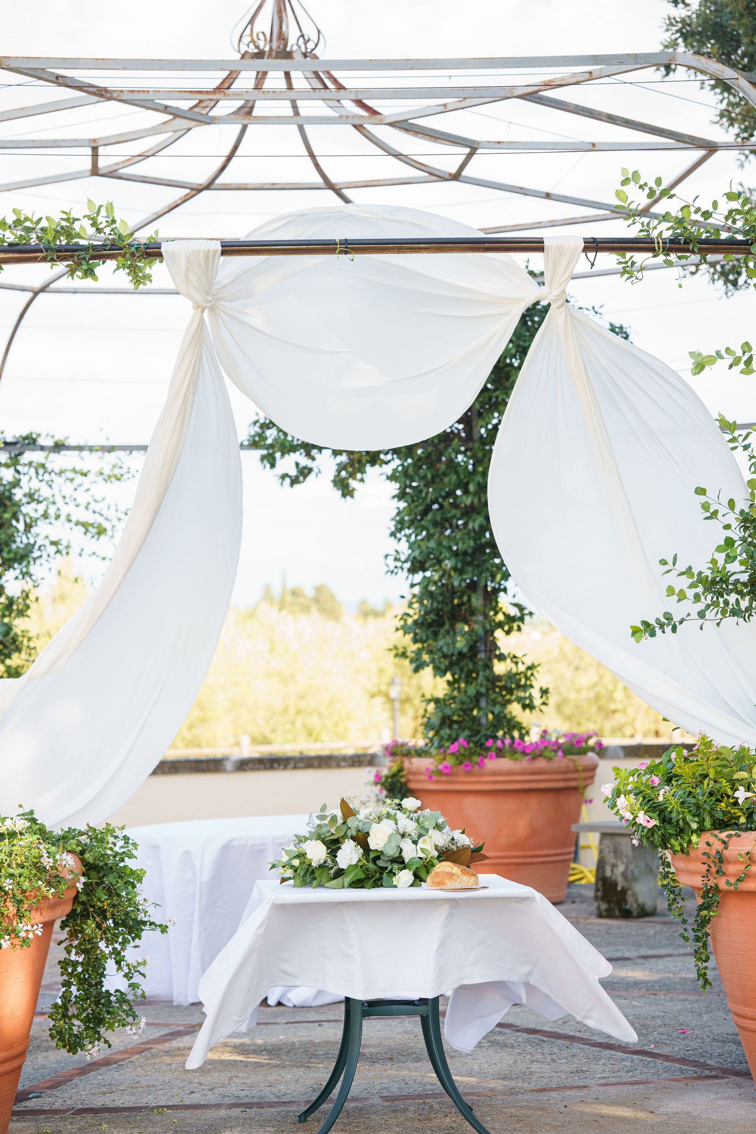 White fabric drapes elegantly from a wooden pergola with terracotta planters in an outdoor garden setting.