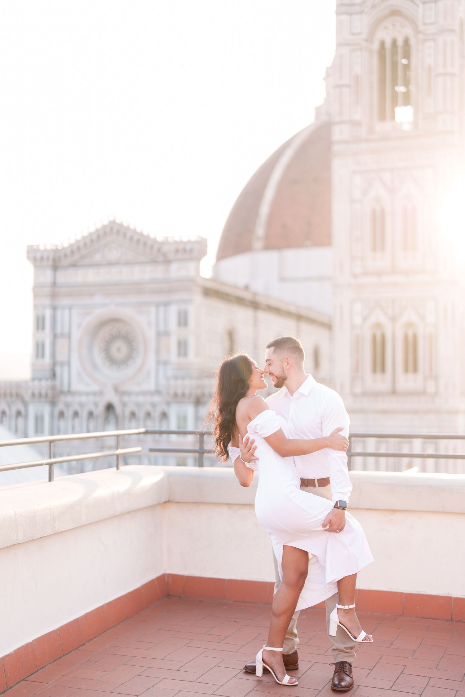 A romantic couple dances together on a rooftop terrace with a beautiful cathedral dome visible in the background.