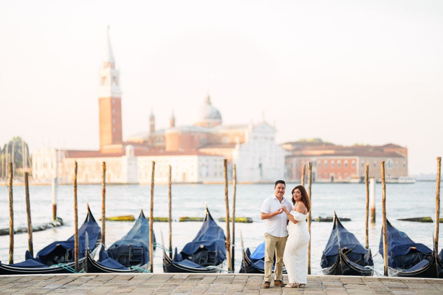 A row of traditional gondolas moored along Venice's waterfront with the iconic city skyline and church domes in the background.