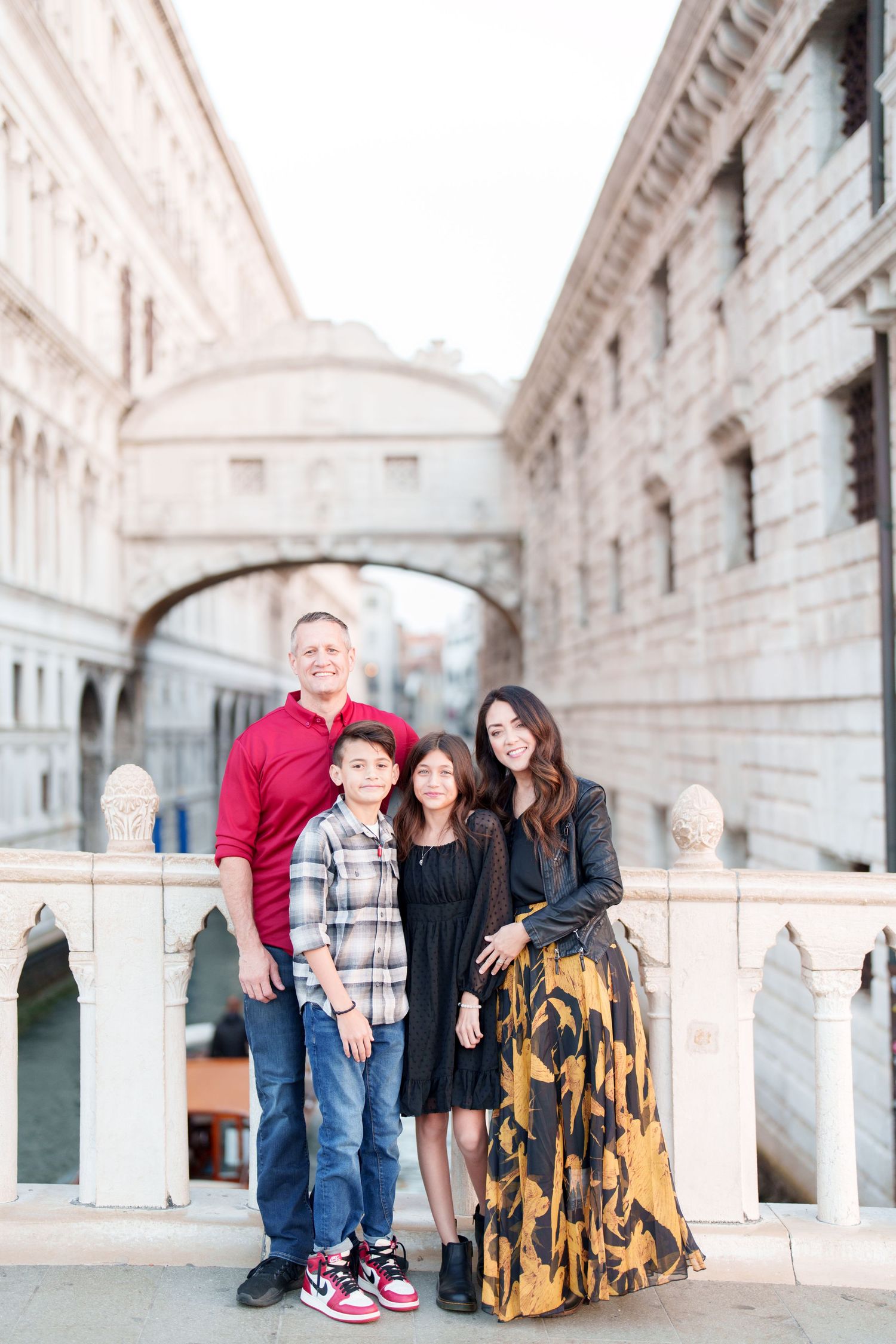 Family posing together on a bridge with ornate stone architecture and arches in Venice, Italy.