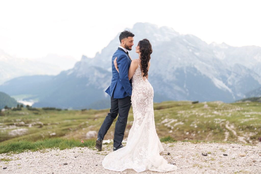 A wedding couple shares a romantic moment on a mountain plateau with dramatic alpine peaks.