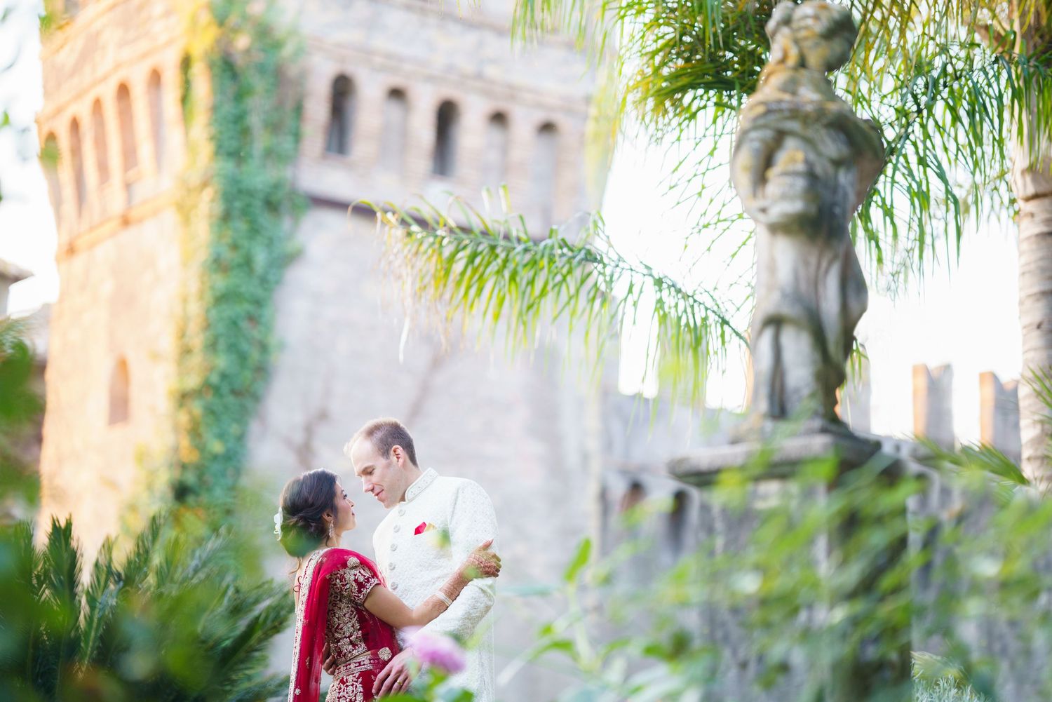 Wedding couple embracing at historic villa with ivy-covered walls and palm trees.