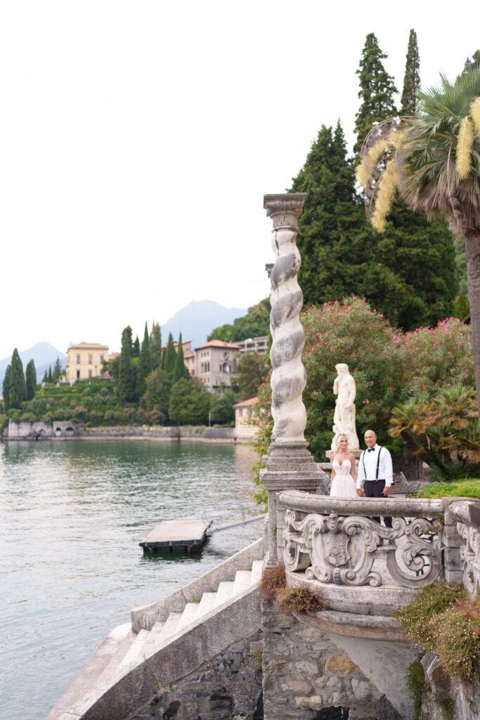 Elegant stone balustrade with classical statues overlooking Lake Como in Italy with mountains in background.
