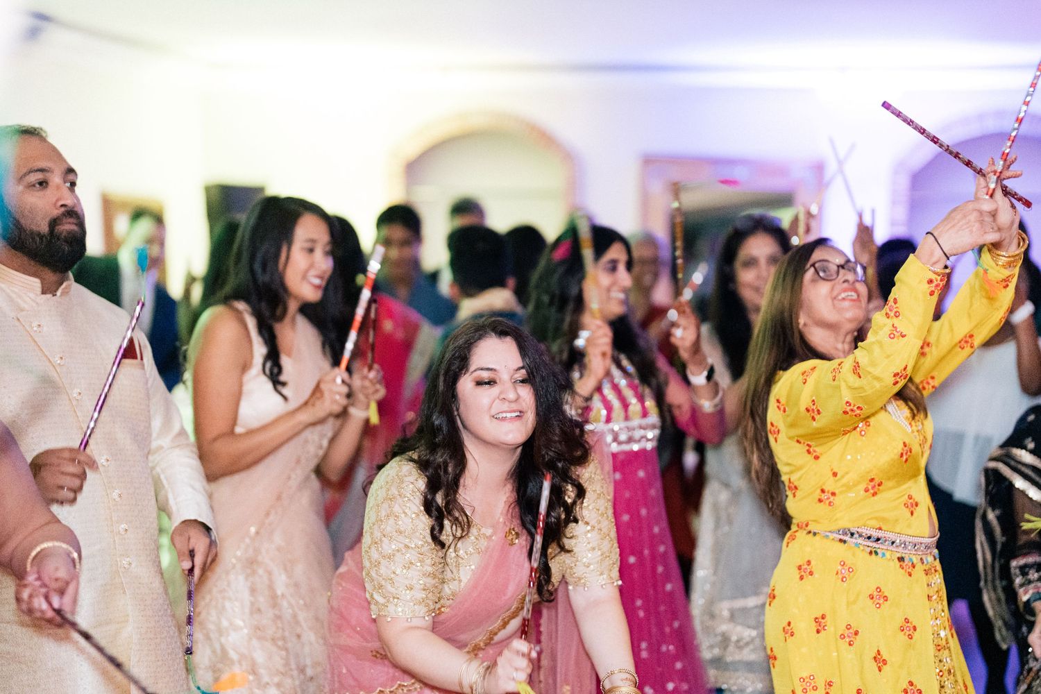 Party guests in colorful outfits dancing and celebrating with sparklers indoors.
