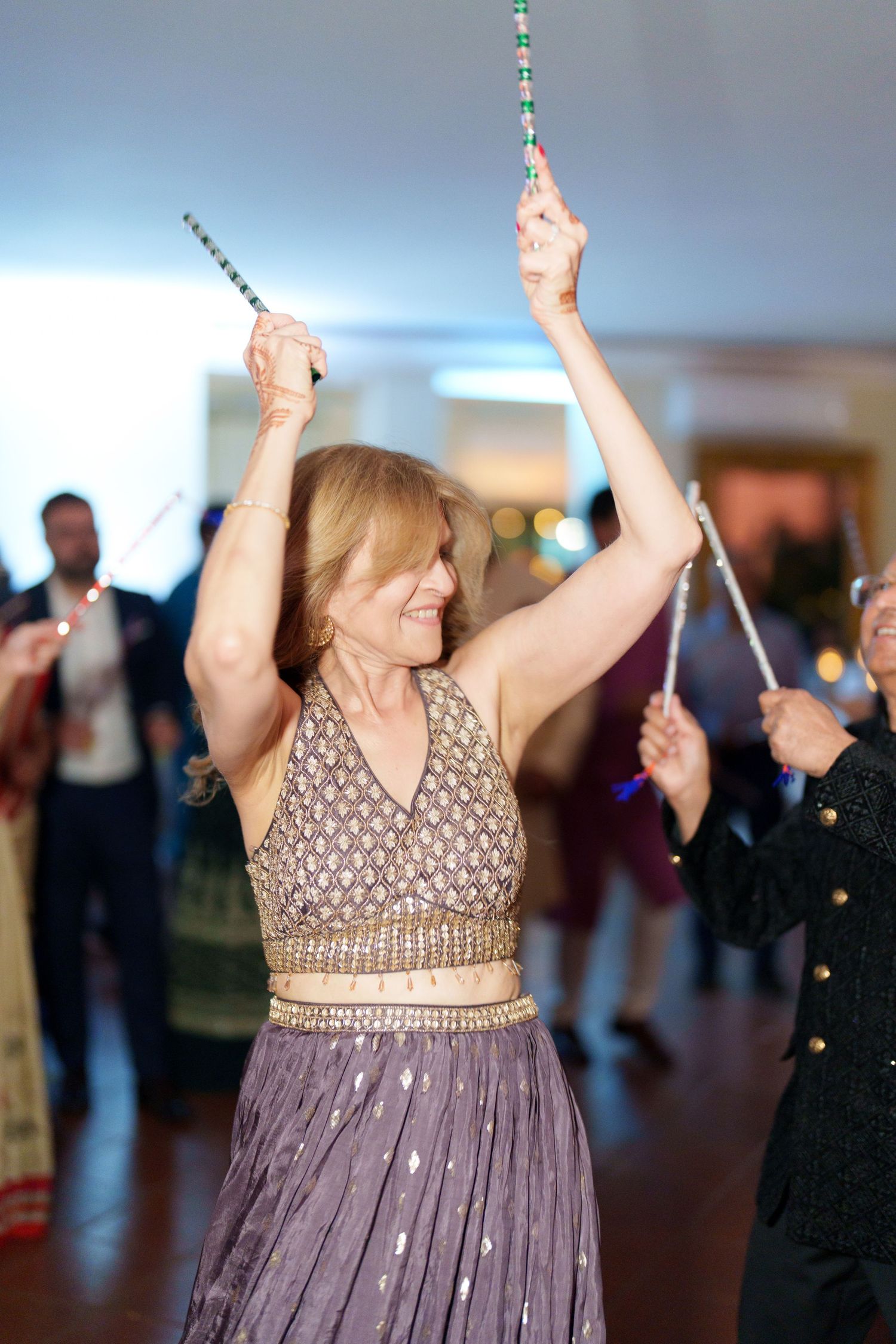 Guest in a purple dress dancing joyfully with sparklers at an indoor celebration.