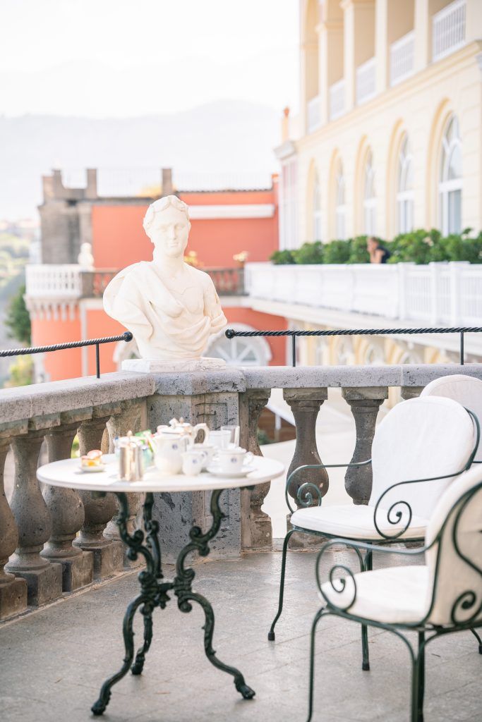 Elegant white wrought iron chairs and tables arranged on a Mediterranean-style terrace with stone balustrades.