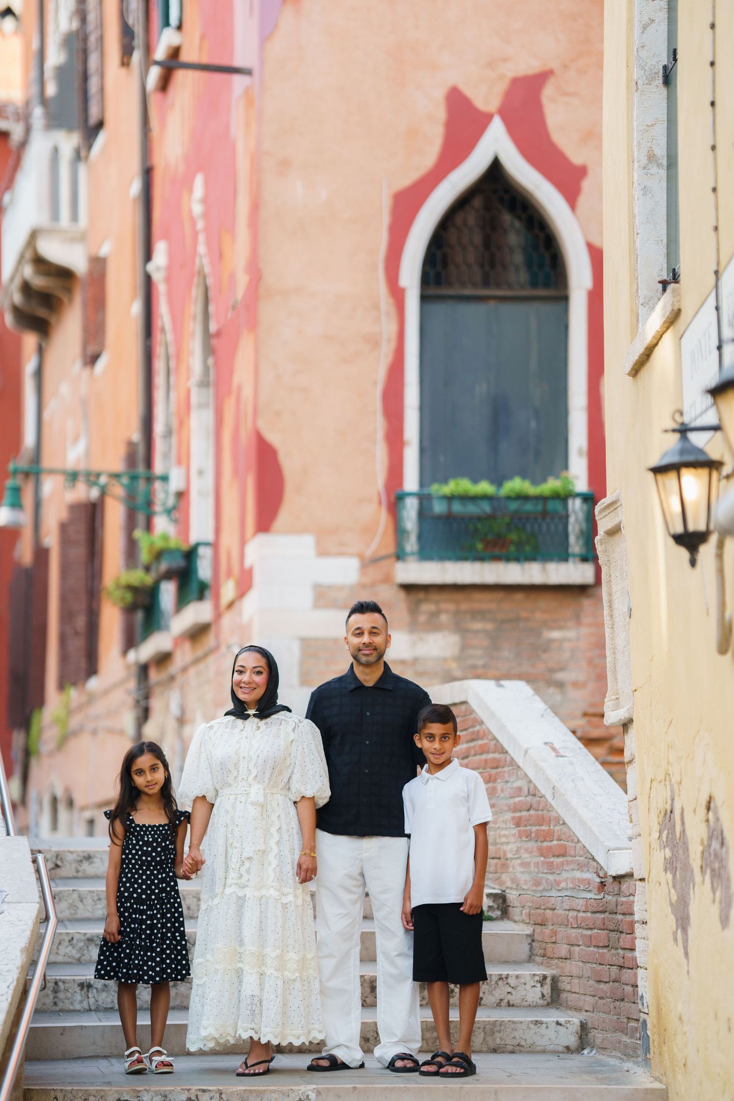 Family of four posing on steps in Venice, Italy, with colorful historic buildings in the background.