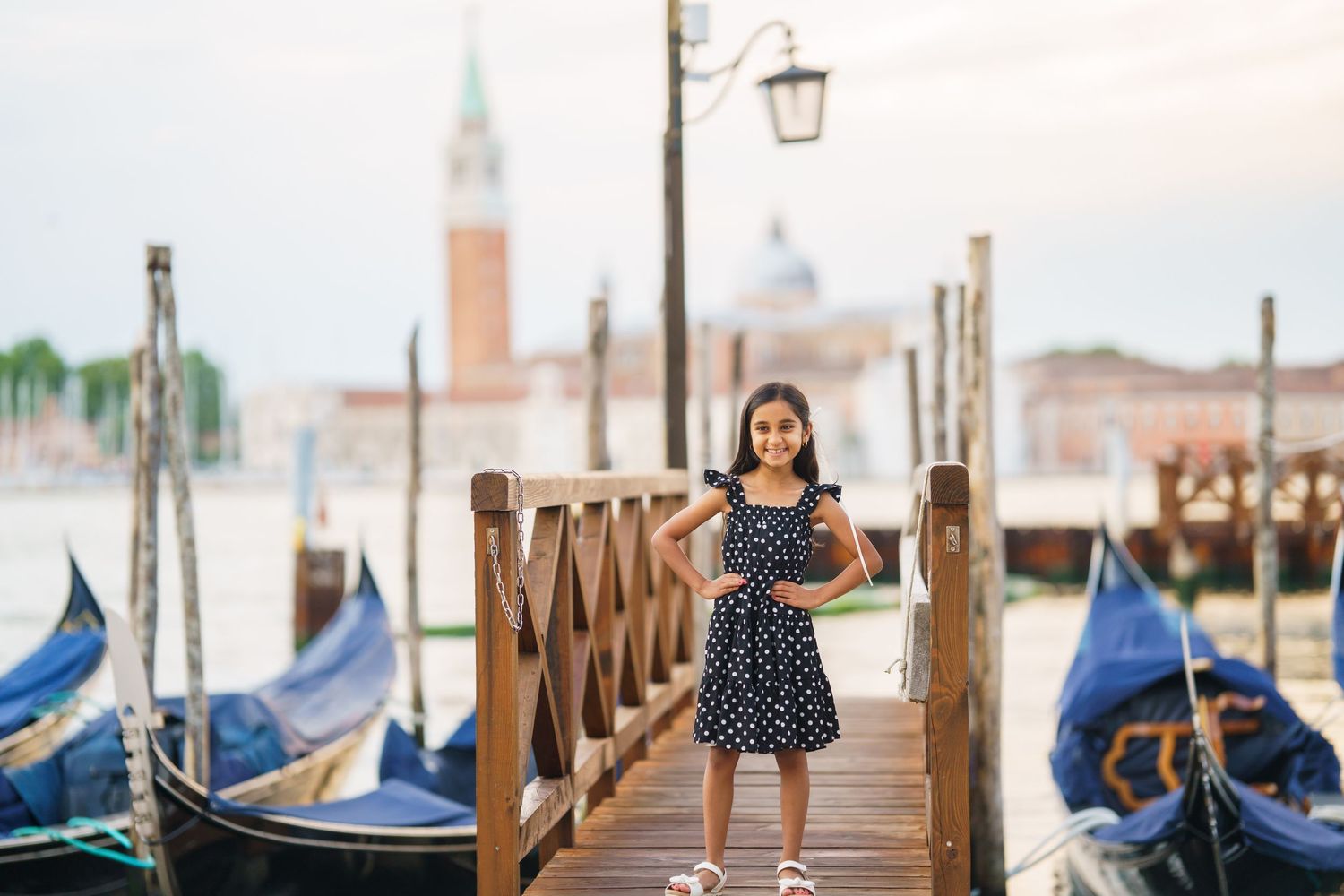 Girl in polka dot dress posing on Venice gondola dock with San Giorgio Maggiore church in background.