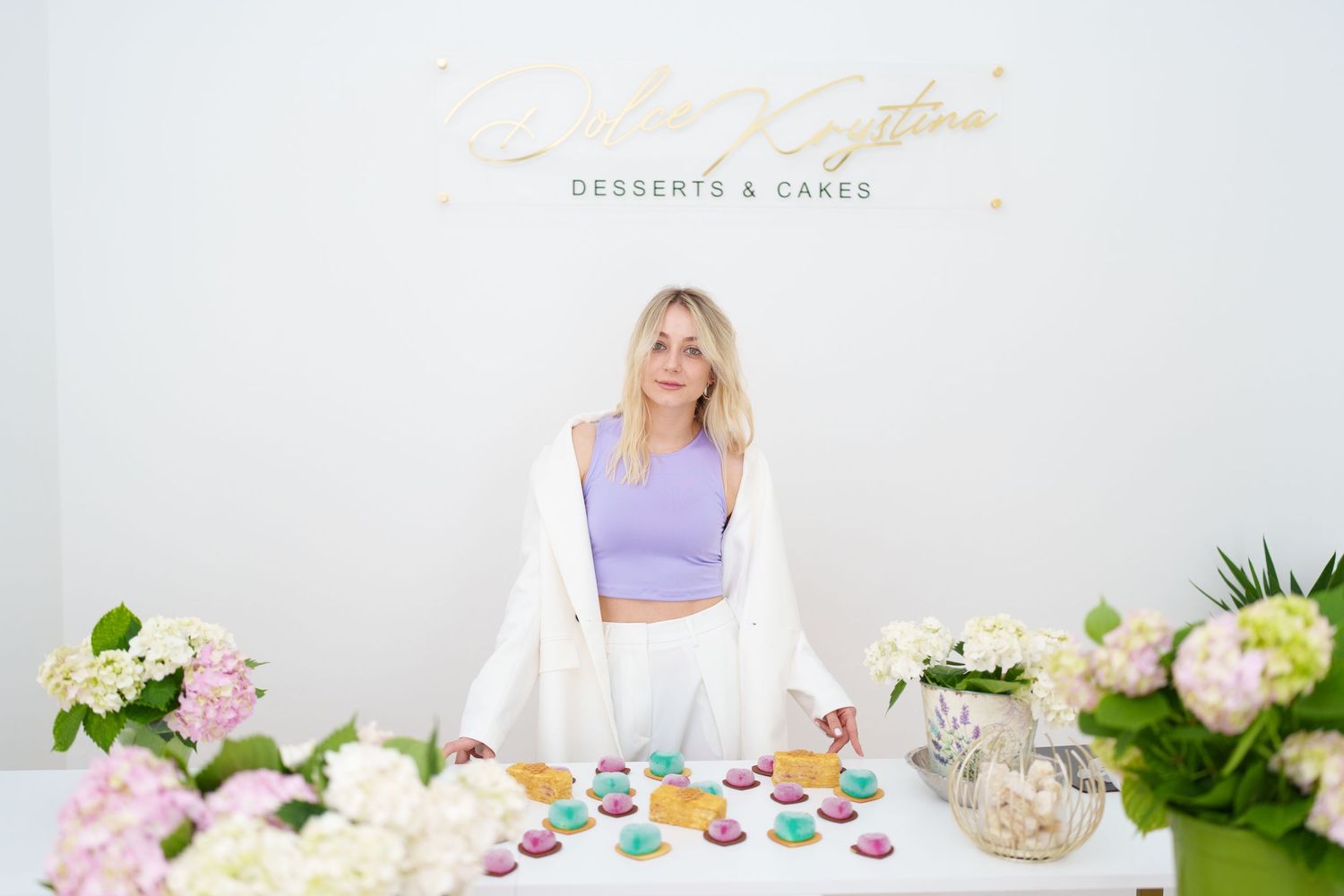 Woman stands behind dessert table with colorful macarons and flowers at Silvana Gastini Desserts and Cakes event.