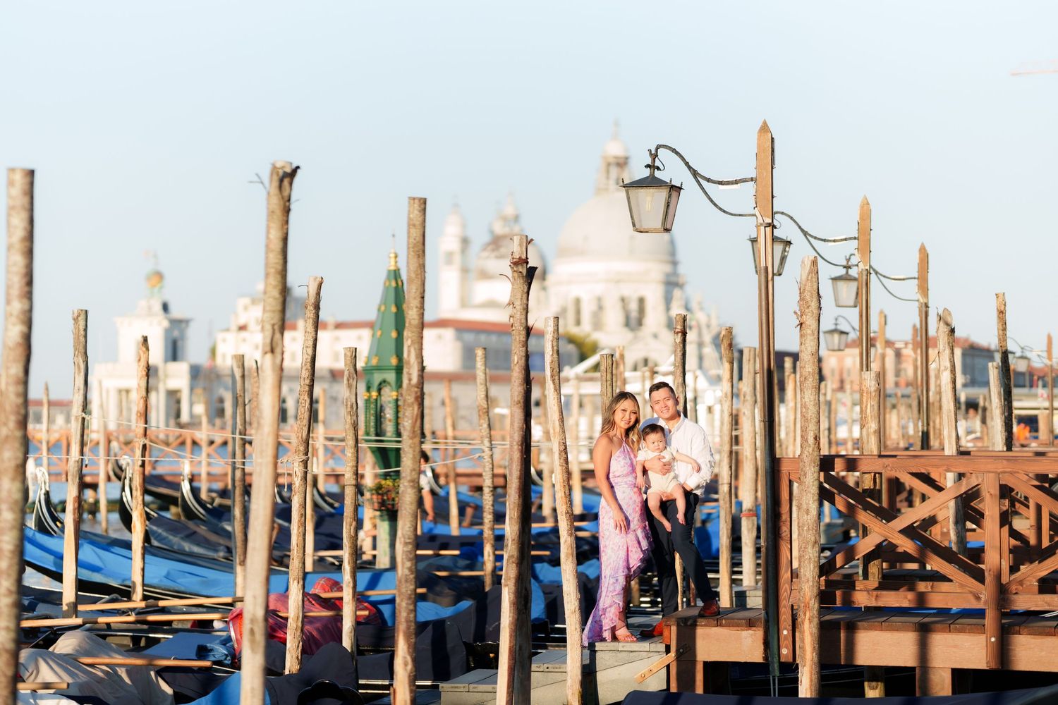 Family posing on Venice gondola dock with Santa Maria della Salute basilica in background at golden hour.