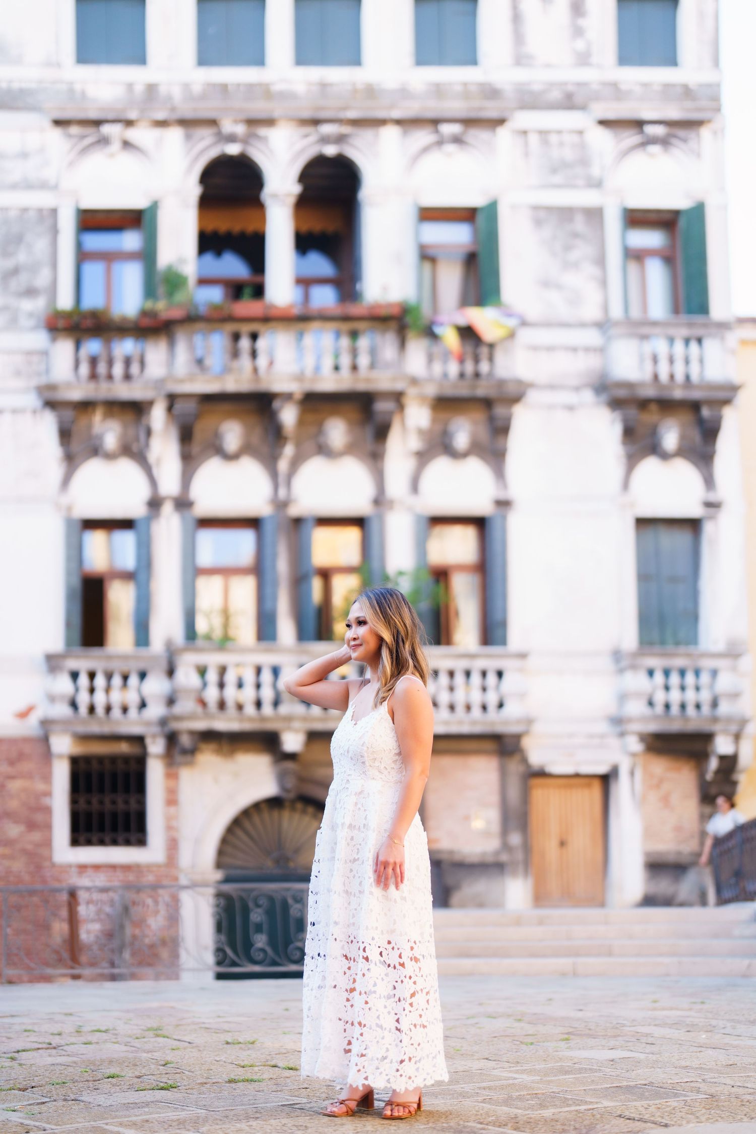 Woman in white lace maxi dress posing in front of ornate Venetian building in Venice, Italy.