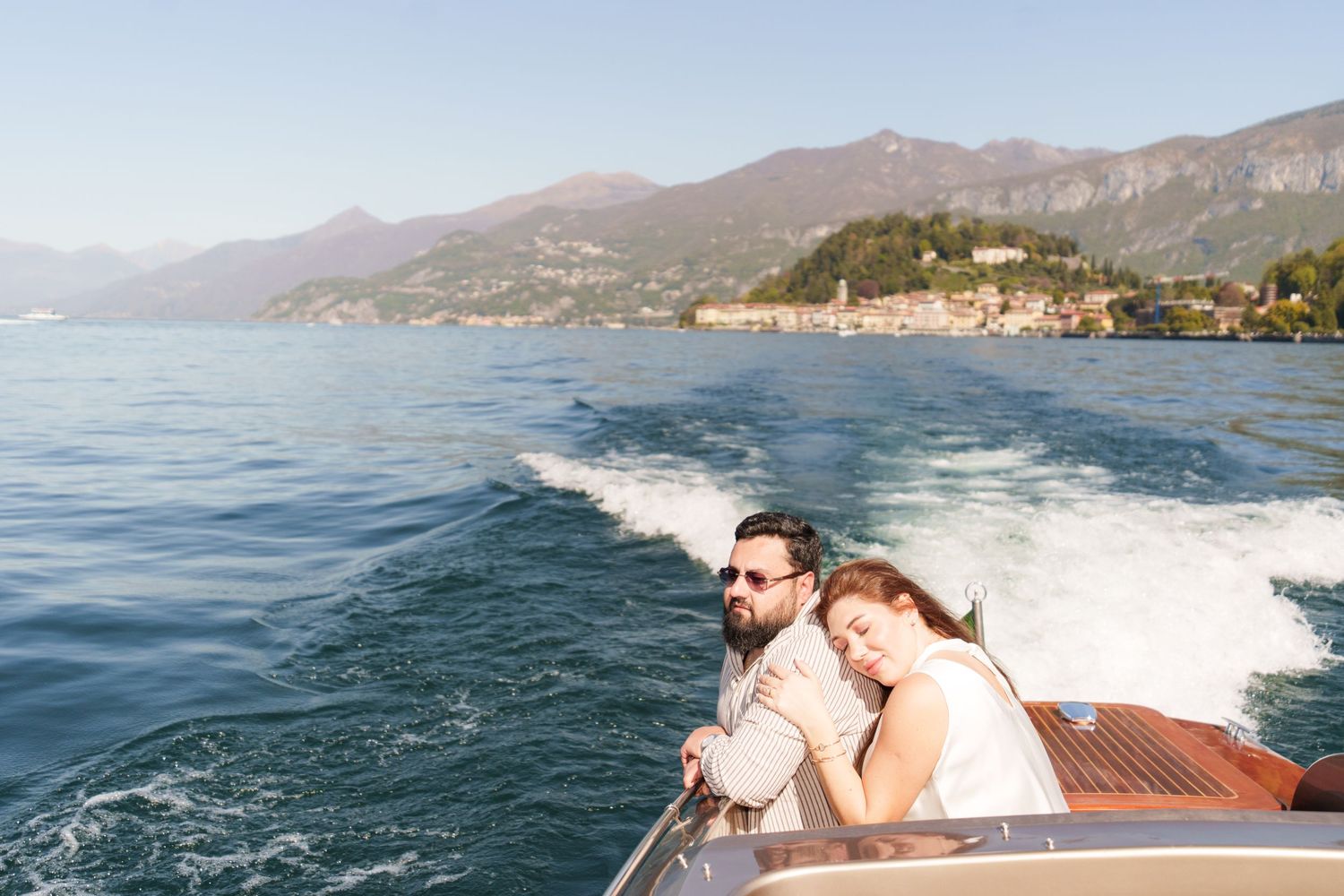 Couple enjoying a scenic boat ride on Lake Como, Italy, with mountains and a village in the background.