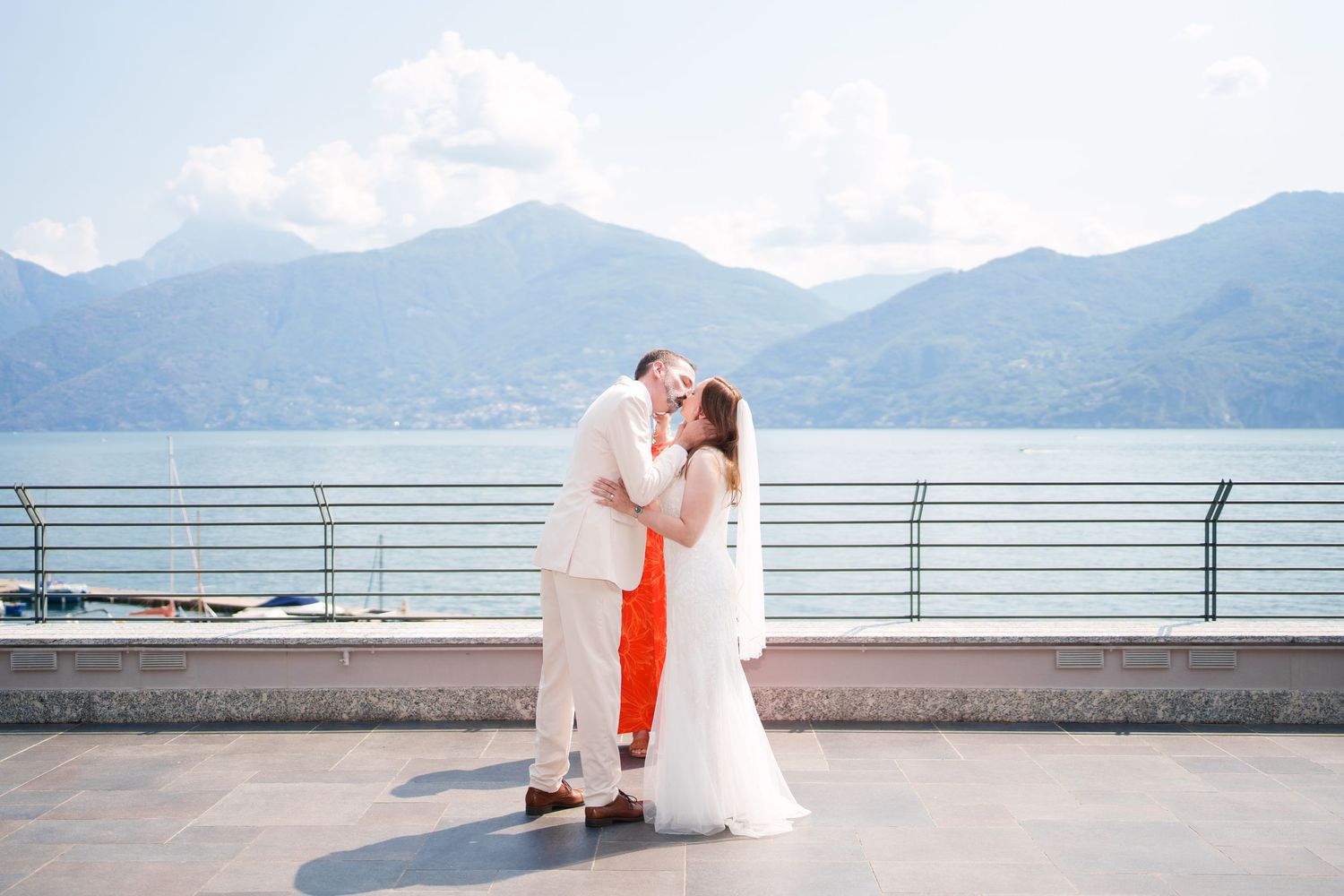Couple sharing a romantic kiss on a lakeside terrace with stunning mountain backdrop at their outdoor wedding.