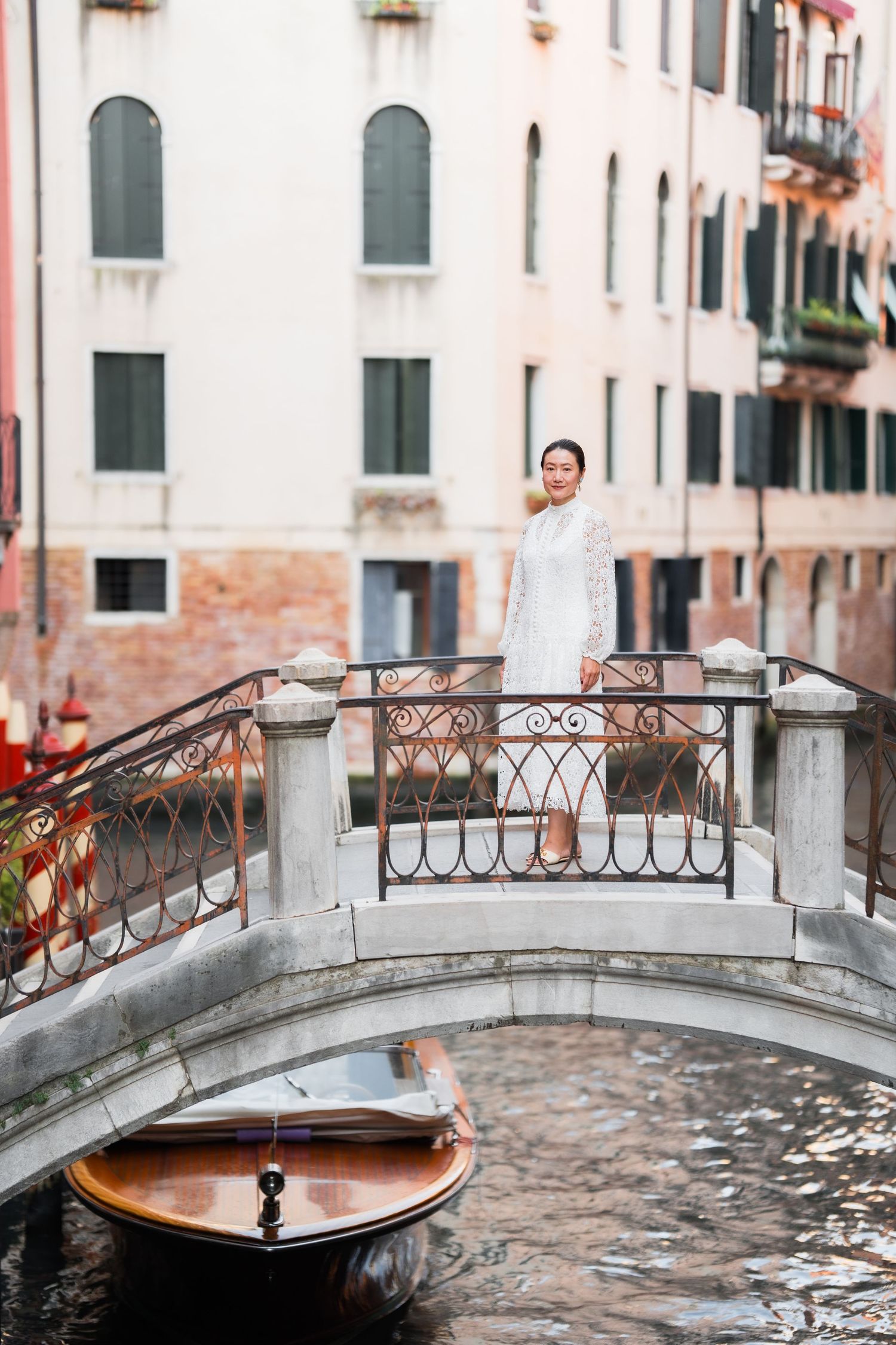 Woman in white dress standing on a charming Venice canal bridge with gondola and historic buildings backdrop.