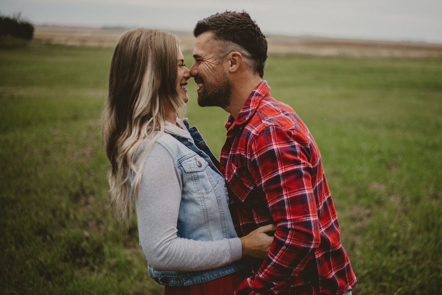 An intimate portrait of a couple in casual attire sharing a close moment in a field.