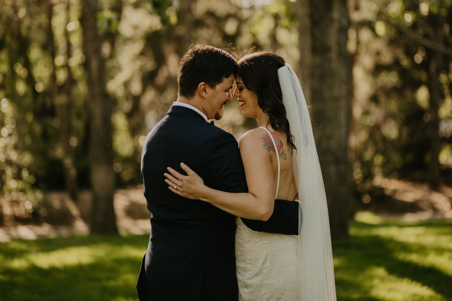 Intimate embrace captured during outdoor wedding photoshoot in sunlit forest setting.