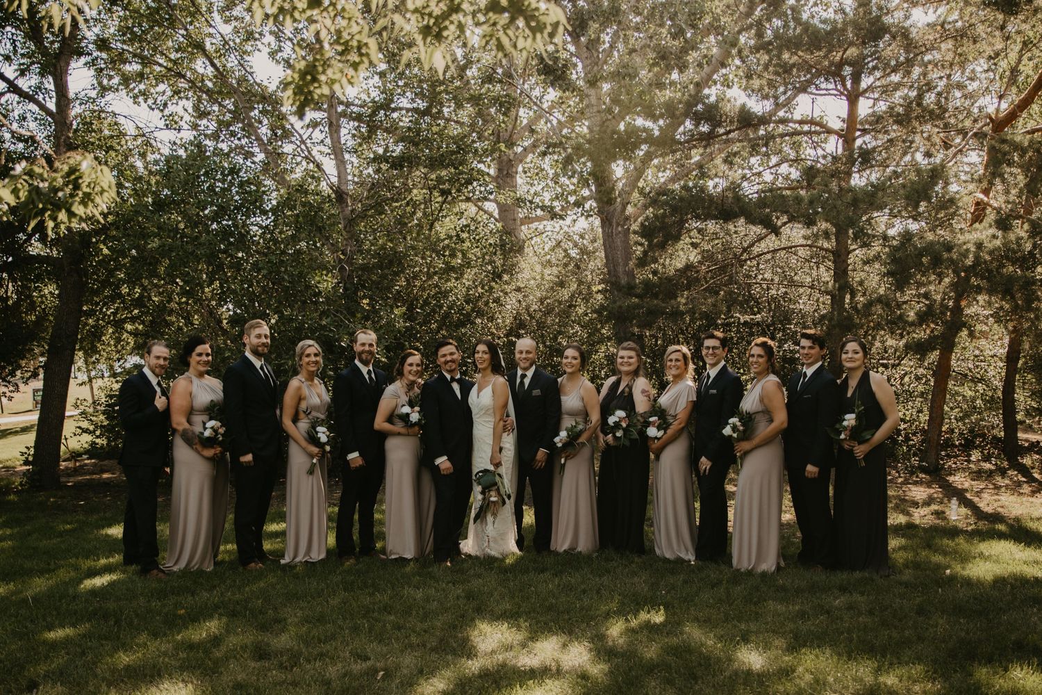 Wedding party lined up on grass with bridesmaids in matching dresses and groomsmen in dark suits.