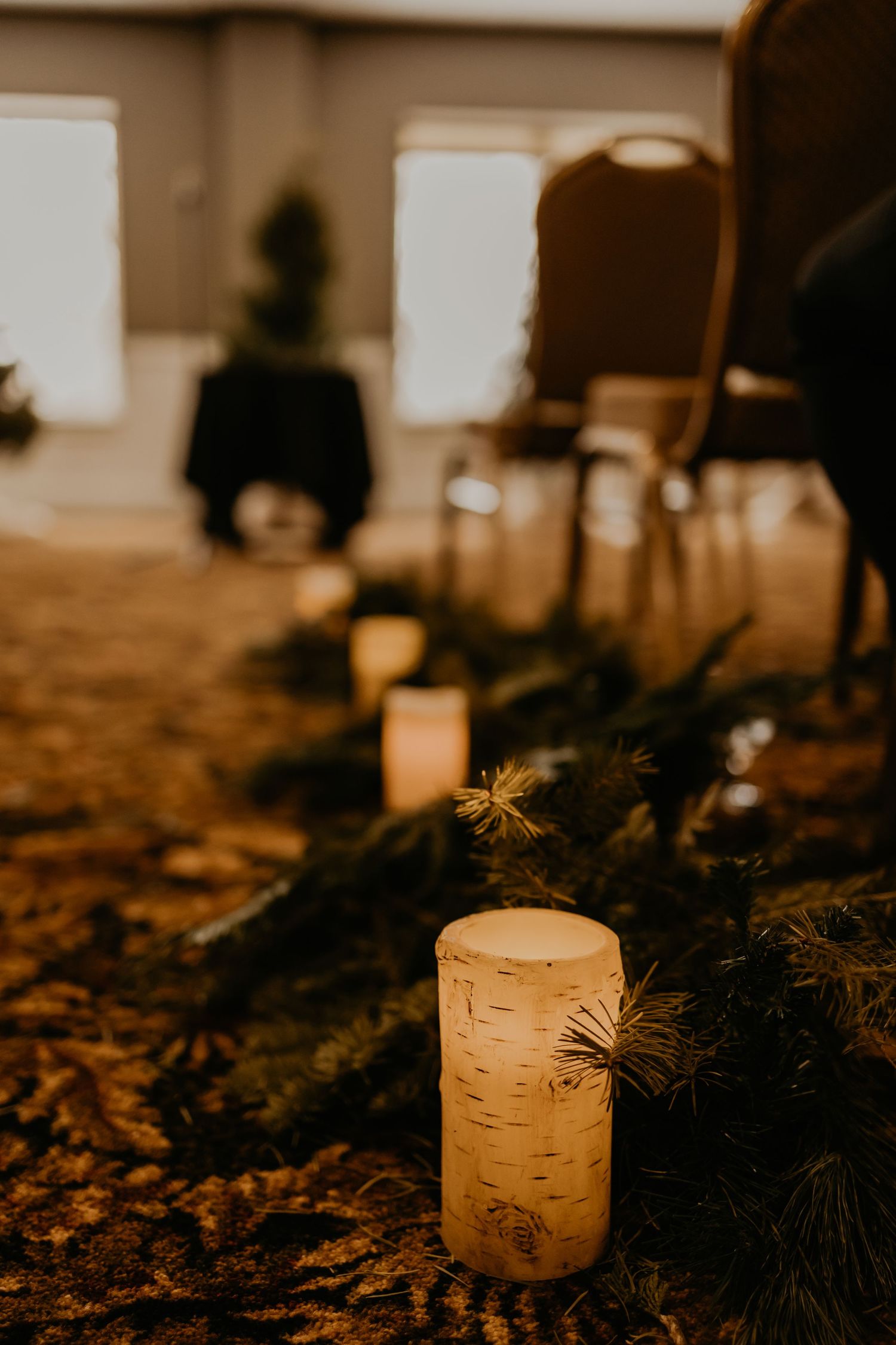 A lit candle with evergreen decorations creates ambiance at a wedding reception.
