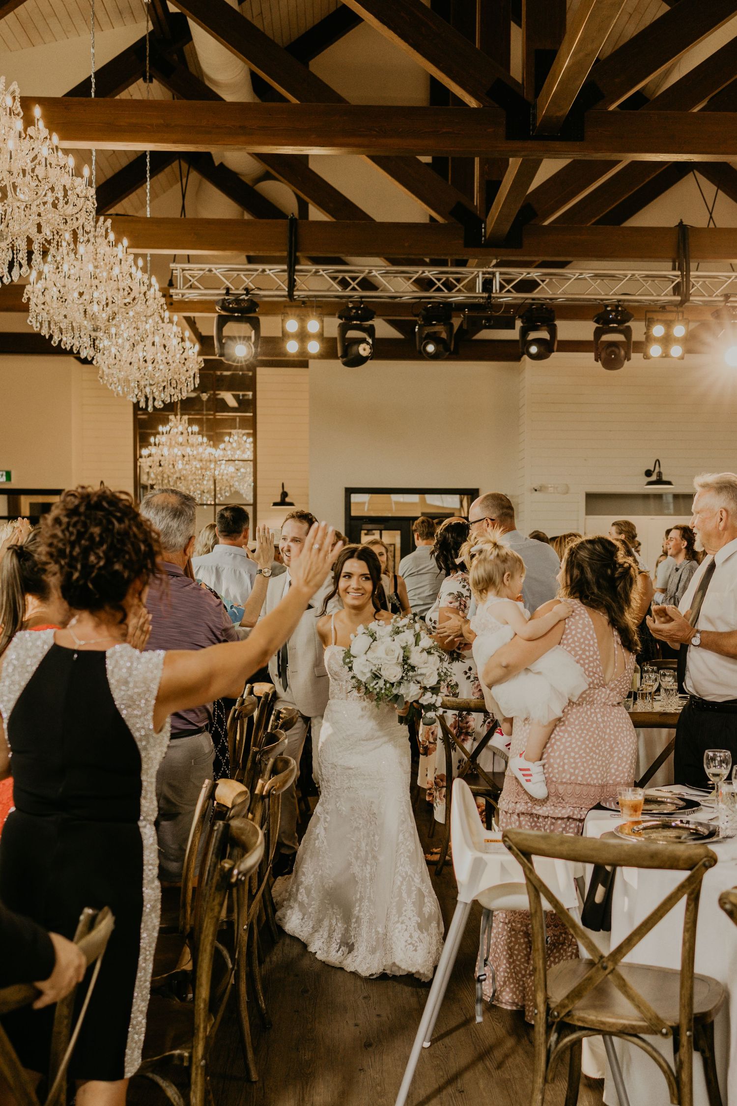 Wedding reception in elegant venue with crystal chandeliers as guests celebrate the newlyweds.